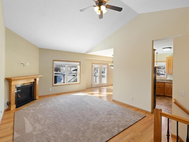 living area featuring baseboards, light wood finished floors, lofted ceiling, a fireplace with flush hearth, and french doors