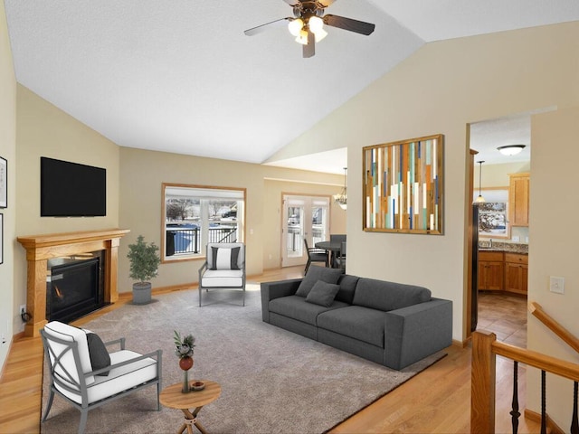 living room featuring baseboards, lofted ceiling, ceiling fan, light wood-style floors, and a glass covered fireplace