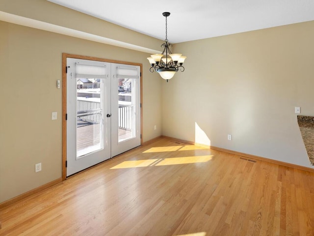 unfurnished room featuring a notable chandelier, light wood-style floors, and french doors