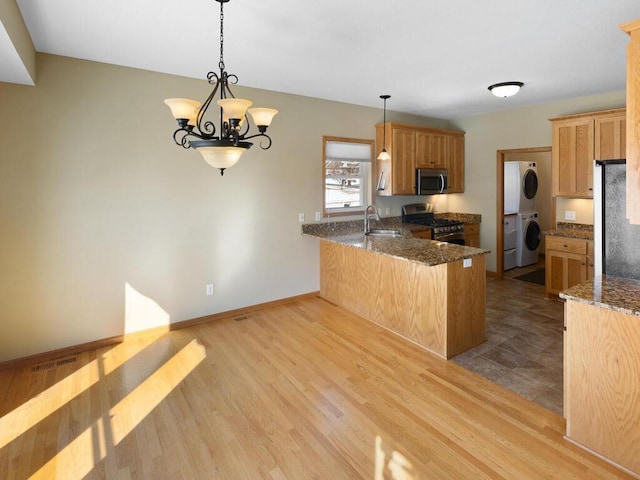 kitchen with wood finished floors, a peninsula, a sink, stacked washer / drying machine, and appliances with stainless steel finishes