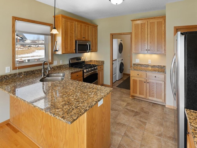 kitchen featuring a sink, stone countertops, stacked washing maching and dryer, appliances with stainless steel finishes, and a peninsula