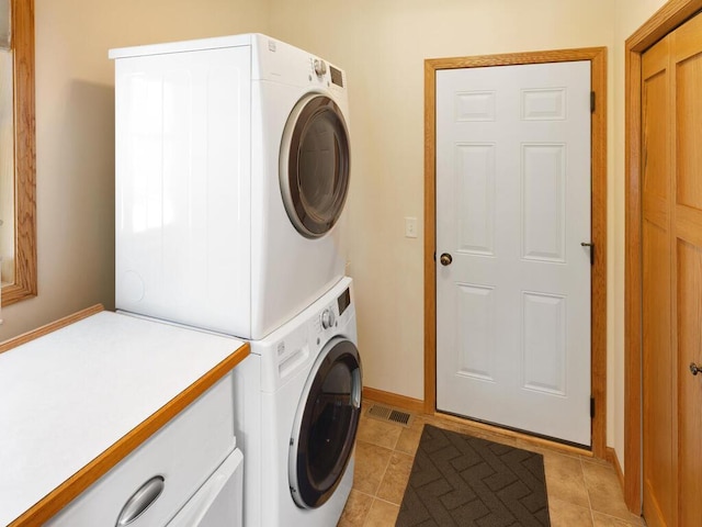 laundry area with light tile patterned floors, stacked washer / dryer, baseboards, and visible vents