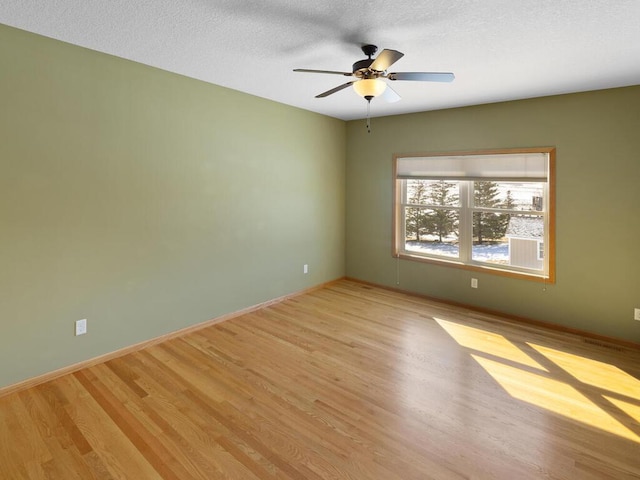 empty room with ceiling fan, baseboards, a textured ceiling, and light wood-style flooring