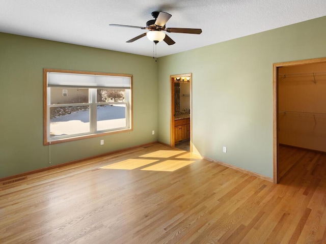 unfurnished bedroom with visible vents, a walk in closet, a closet, light wood finished floors, and baseboards