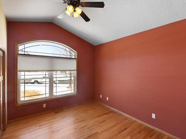 empty room with a ceiling fan, visible vents, vaulted ceiling, a textured ceiling, and light wood-type flooring