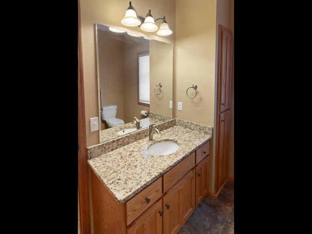 bathroom featuring toilet, vanity, and stone finish floor