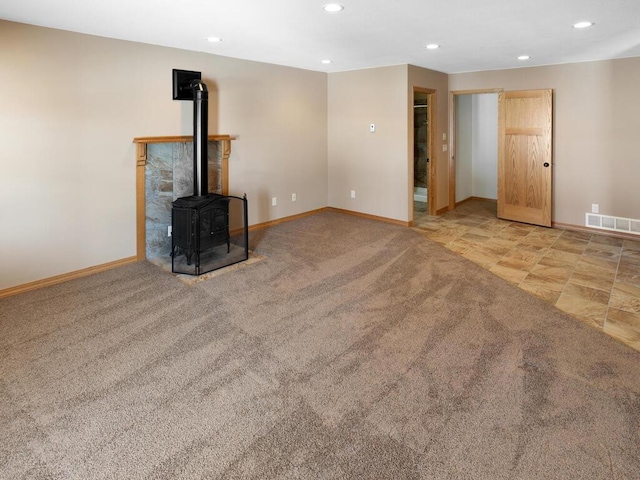 unfurnished living room featuring visible vents, recessed lighting, carpet floors, baseboards, and a wood stove