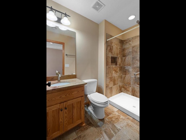 bathroom with visible vents, toilet, vanity, and a tile shower