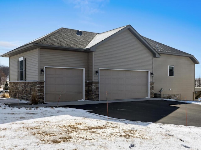 view of snowy exterior with an attached garage and roof with shingles