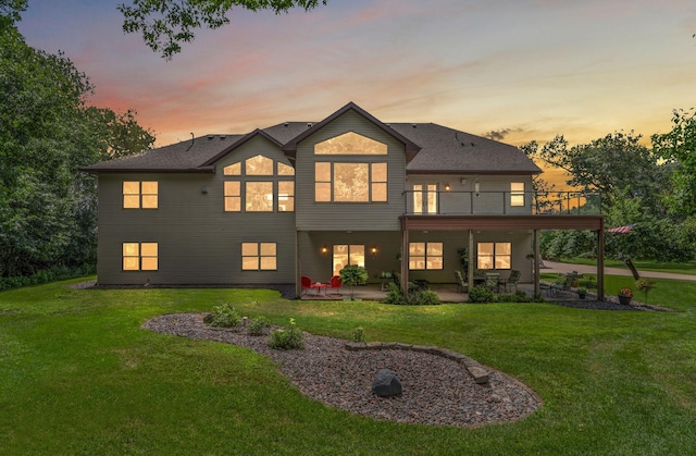 back of house at dusk featuring a lawn and a patio