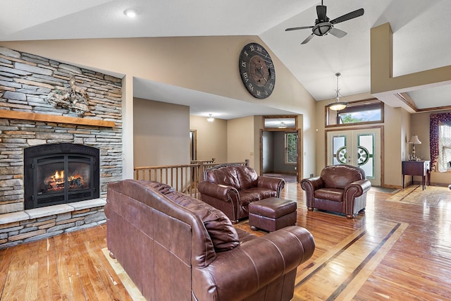 living area featuring light wood finished floors, high vaulted ceiling, french doors, and a stone fireplace