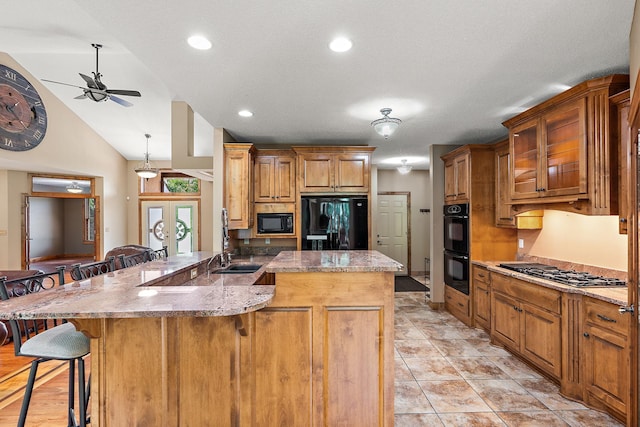 kitchen with a ceiling fan, light stone counters, a breakfast bar, vaulted ceiling, and black appliances