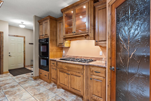 kitchen with light tile patterned floors, glass insert cabinets, brown cabinets, a textured ceiling, and black appliances