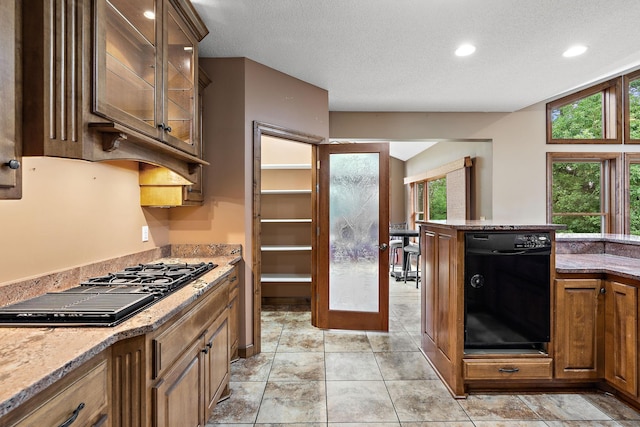 kitchen featuring brown cabinetry, glass insert cabinets, light stone counters, a textured ceiling, and black appliances