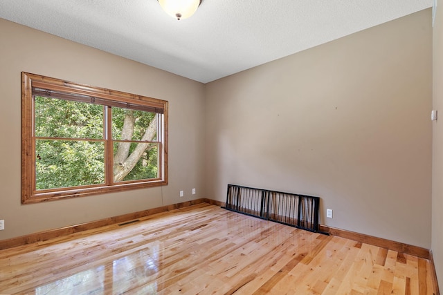 spare room featuring wood-type flooring, visible vents, a textured ceiling, and baseboards