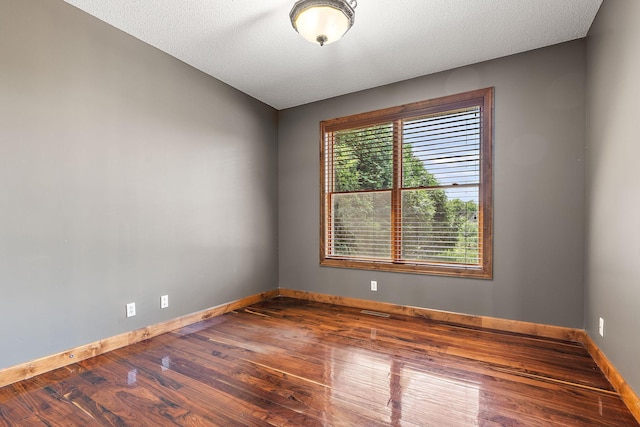 spare room with a textured ceiling, baseboards, and wood finished floors