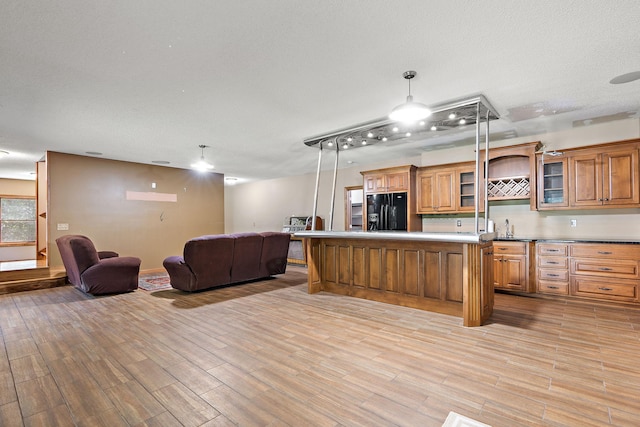 kitchen featuring a kitchen island, light wood-style floors, open floor plan, black fridge, and brown cabinets