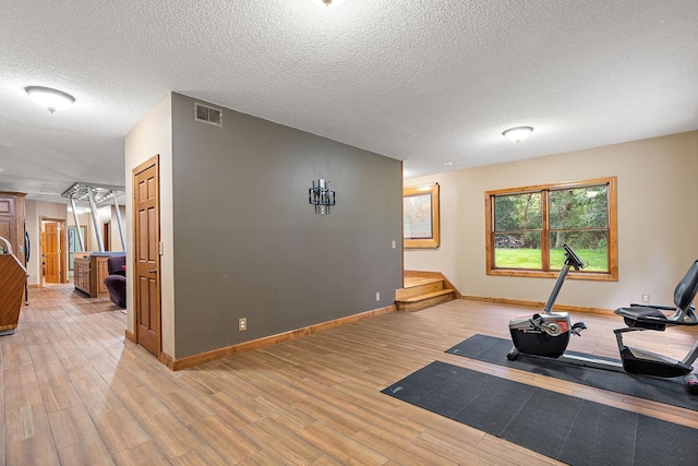 exercise area with baseboards, a textured ceiling, visible vents, and light wood-style floors