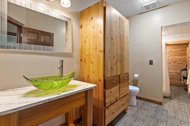 bathroom featuring baseboards, visible vents, toilet, a textured ceiling, and vanity