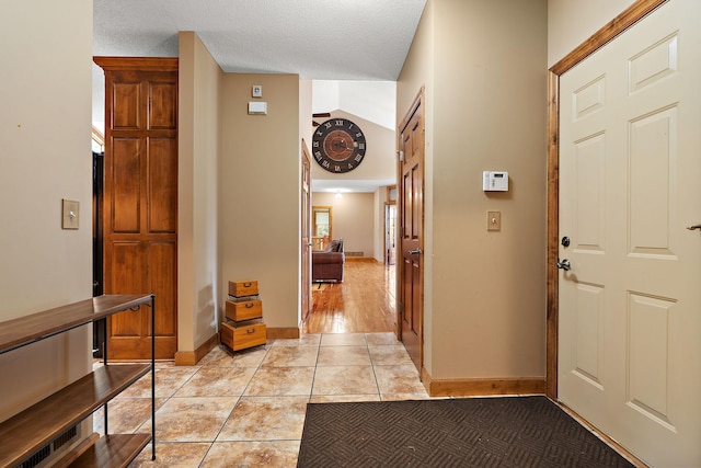 foyer entrance with a textured ceiling, light tile patterned flooring, and baseboards