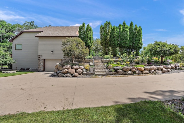 view of side of property with a garage, driveway, stairway, and roof with shingles