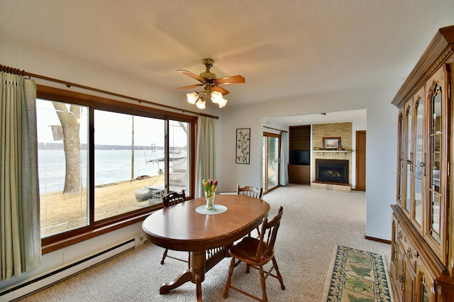 dining area with carpet, a baseboard radiator, ceiling fan, a textured ceiling, and a brick fireplace