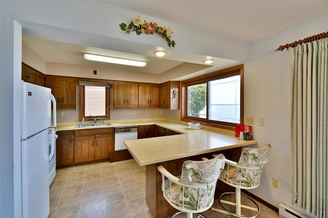 kitchen featuring a baseboard radiator, light countertops, a peninsula, white appliances, and a sink