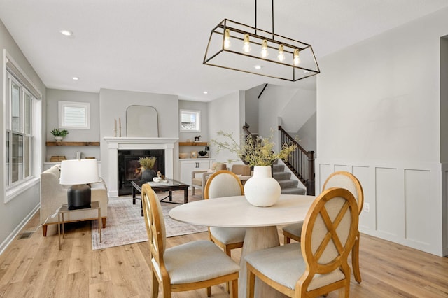 dining space featuring a glass covered fireplace, a wainscoted wall, stairway, light wood-style floors, and recessed lighting