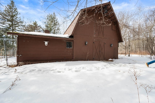 view of snowy exterior with a barn, a garage, and an outbuilding