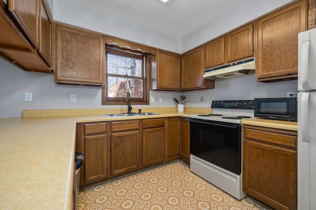 kitchen featuring black microwave, under cabinet range hood, range with electric stovetop, a sink, and freestanding refrigerator