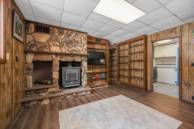 unfurnished living room featuring a wood stove, visible vents, wooden walls, and wood finished floors