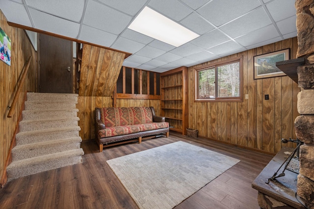 living area with wood walls, stairway, a drop ceiling, and wood finished floors