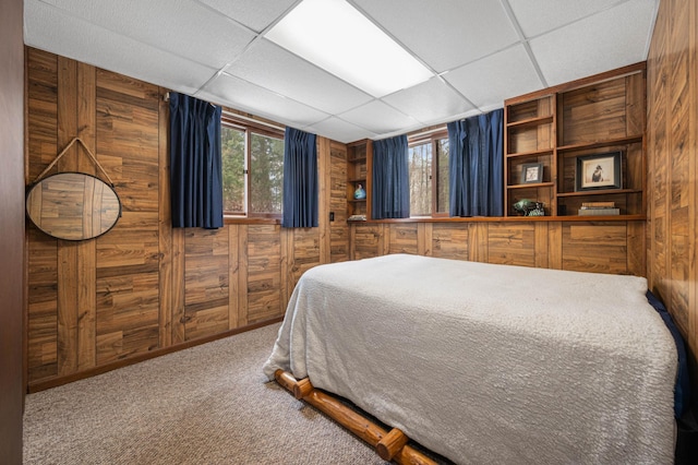 bedroom with carpet floors, wooden walls, and a drop ceiling