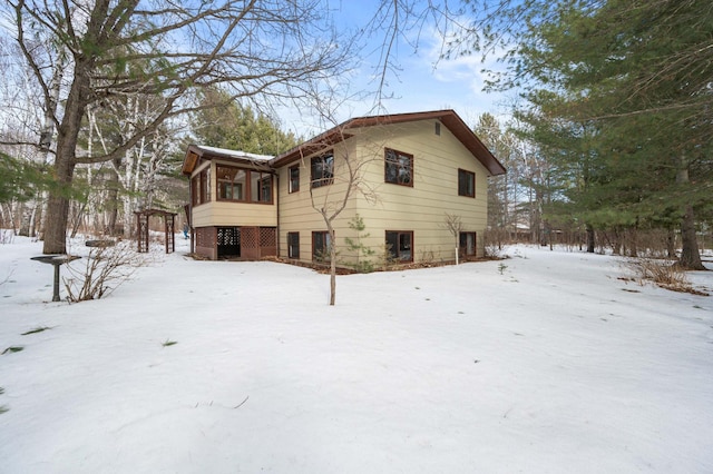 snow covered rear of property featuring a sunroom and brick siding