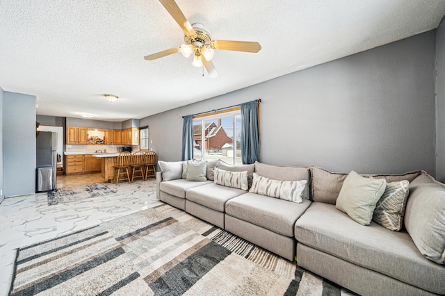 living area featuring a textured ceiling, marble finish floor, and ceiling fan