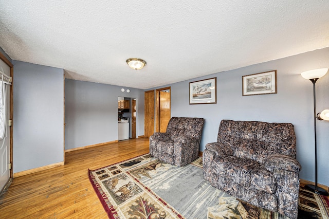 living area with baseboards, a textured ceiling, and wood finished floors