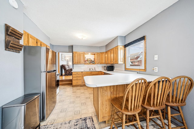 kitchen featuring a peninsula, a sink, light countertops, appliances with stainless steel finishes, and a textured ceiling