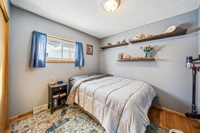 bedroom with baseboards, wood finished floors, visible vents, and a textured ceiling