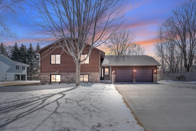 view of front of property featuring brick siding, an attached garage, driveway, and fence