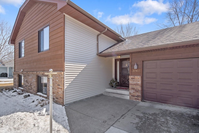 view of snowy exterior featuring an attached garage, brick siding, and a shingled roof