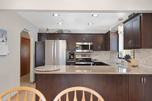 kitchen featuring dark brown cabinetry, light stone counters, a peninsula, stainless steel appliances, and a sink