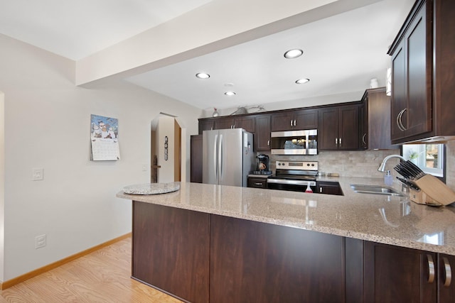 kitchen with a sink, tasteful backsplash, appliances with stainless steel finishes, a peninsula, and dark brown cabinets