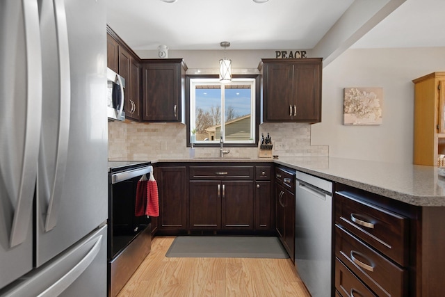 kitchen with a sink, stainless steel appliances, dark brown cabinetry, a peninsula, and light wood finished floors