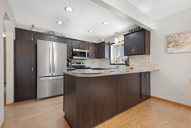 kitchen featuring light wood-type flooring, backsplash, stainless steel appliances, a peninsula, and dark brown cabinets