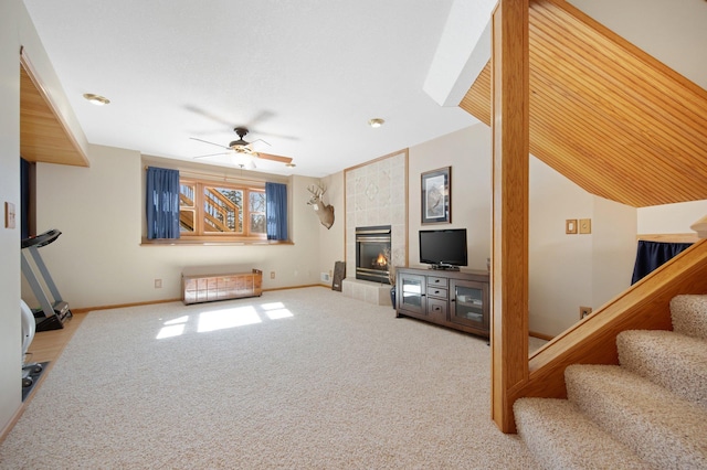 living area featuring carpet, baseboards, a fireplace, ceiling fan, and stairs