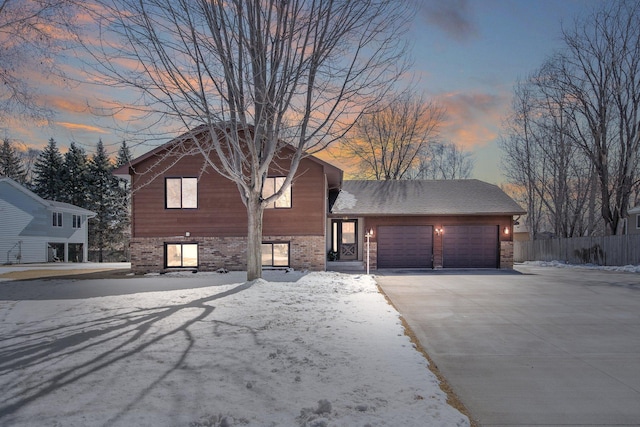 view of front of property featuring brick siding, driveway, an attached garage, and fence