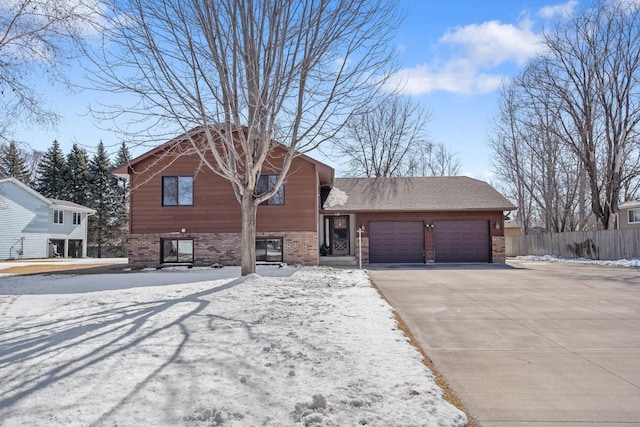 view of front facade featuring driveway, fence, roof with shingles, a garage, and brick siding