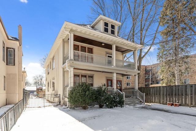 american foursquare style home featuring a balcony, fence, and covered porch