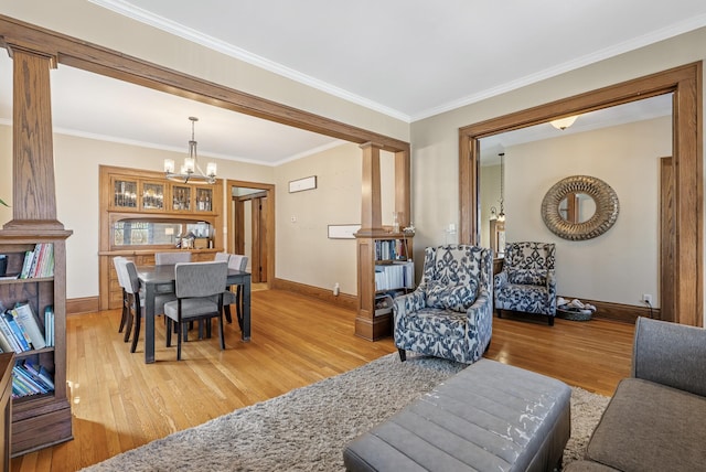 living room featuring light wood finished floors, crown molding, baseboards, an inviting chandelier, and ornate columns