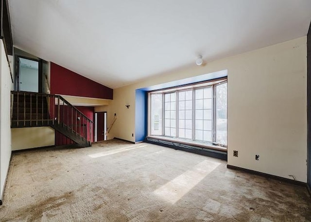 unfurnished living room featuring carpet flooring, vaulted ceiling, stairway, and baseboards